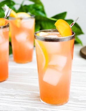 A close up of a glass of peach lemonade in front of 2 more glasses of the lemonade.