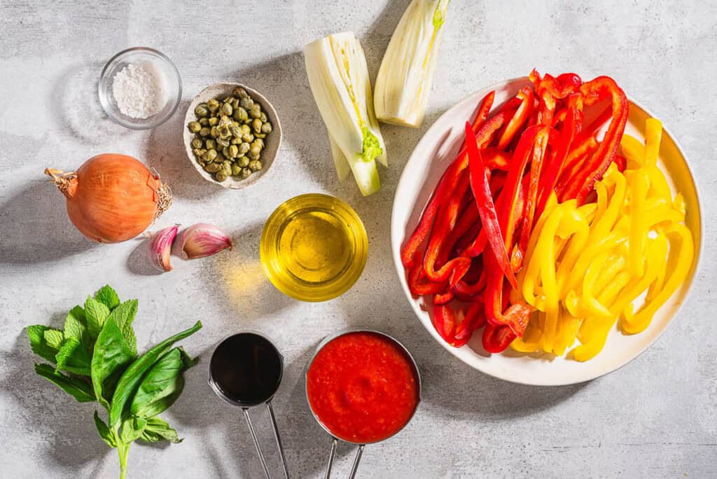 Ingredients for peperonata including bell peppers, olive oil, onion, fennel, garlic, salt, tomato sauce, capers, balsamic vinegar, basil and mint.