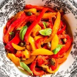 An overhead photo of peperonata in a bowl. Next to this is a glass and slices of grilled bread.