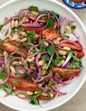 Turkish white bean salad with onions and tomatoes on a deep white plate with sumac alongside.