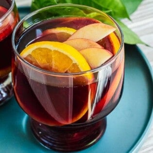 close up of a glass of red sangria with sliced apples and oranges.