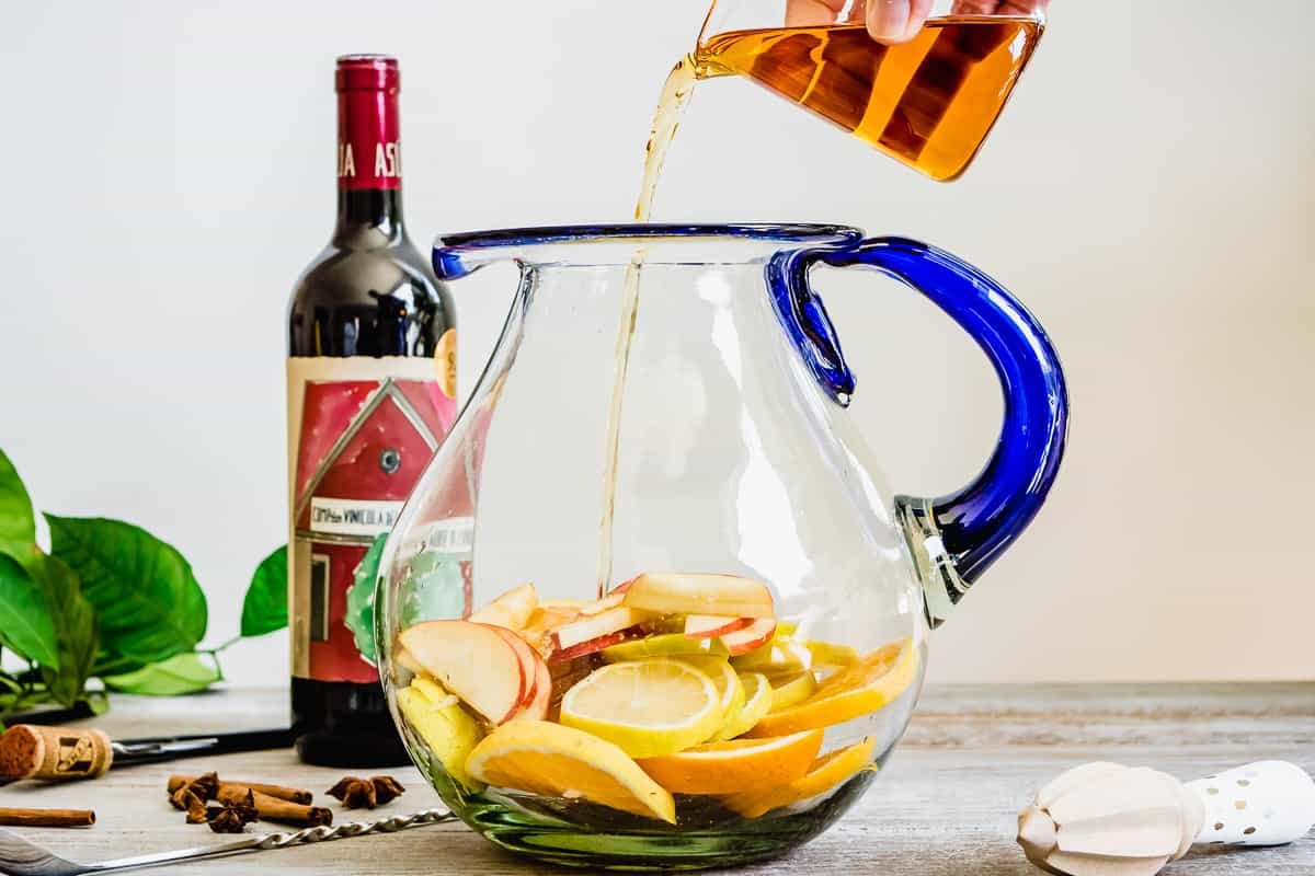 brandy being poured into a pitcher with sliced apples and oranges.