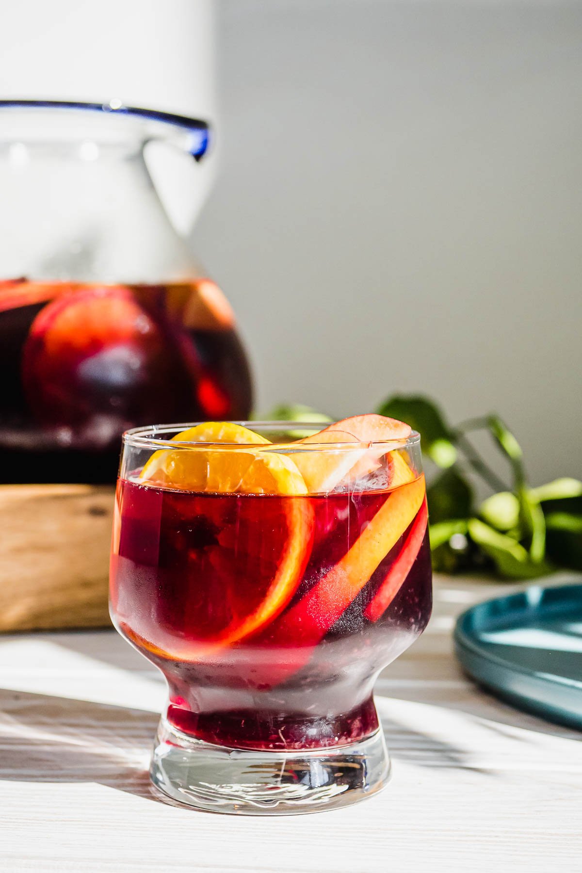 a glass of red sangria with a pitcher of red sangria in the background.