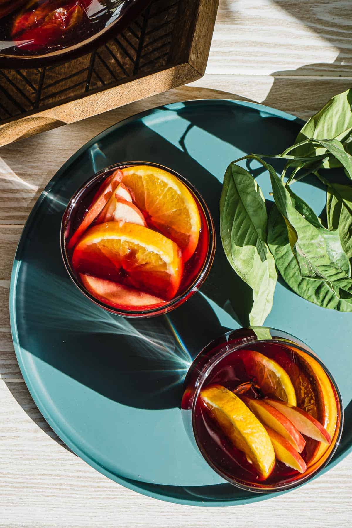 overhead view of two glasses of red sangria and sliced apples and oranges.