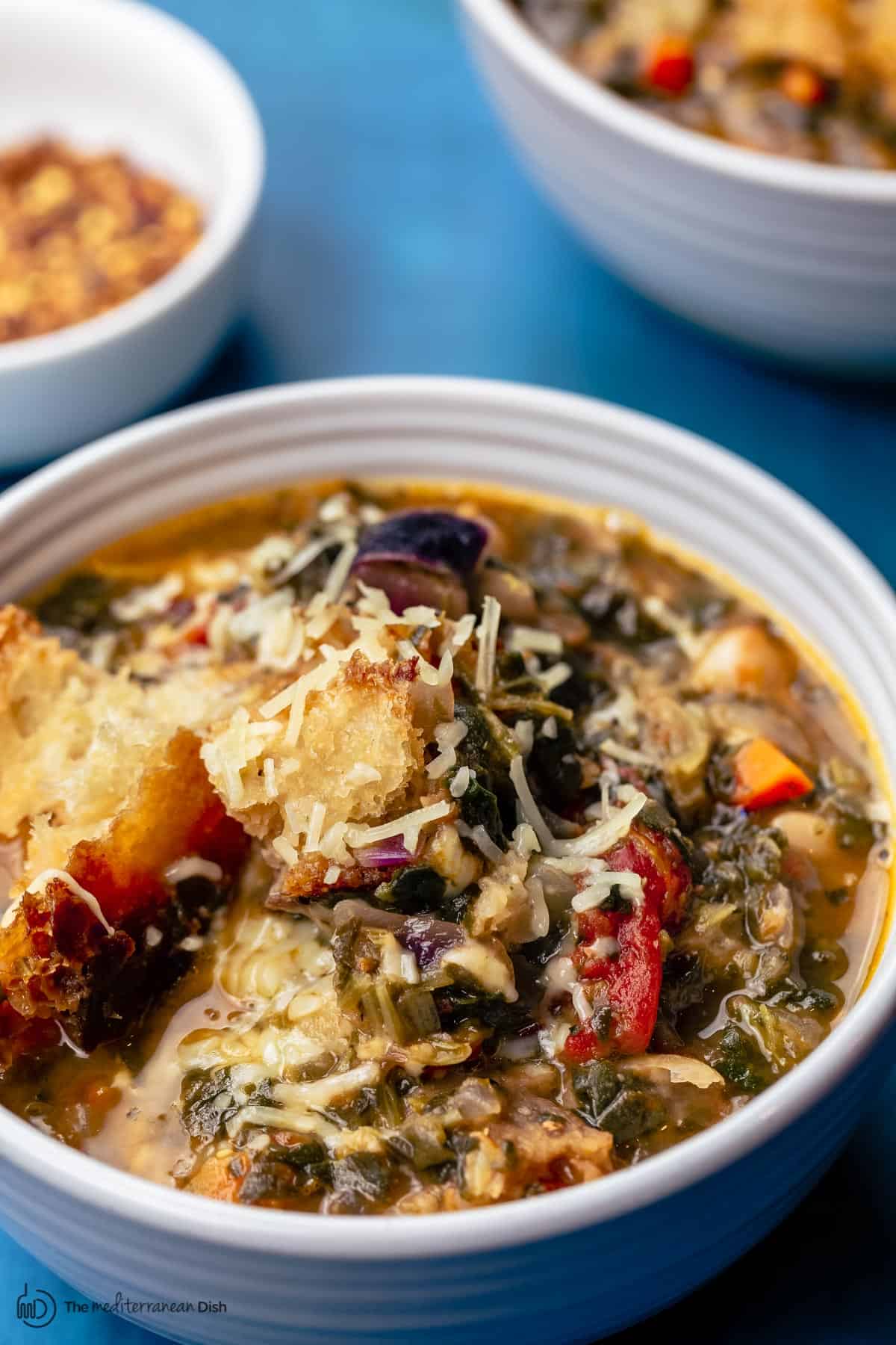 Ribollita in serving bowls with a side of crushed red pepper flakes