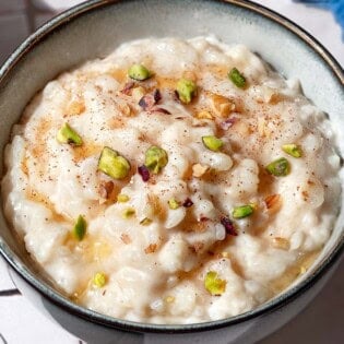 A close up of easy rice pudding garnished with pistachios, walnuts, cinnamon and a drizzle of honey.