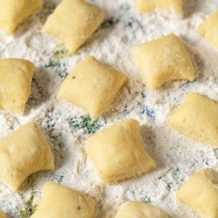 a close up of ricotta gnocchi pieces on a towel sprinkled with flour.