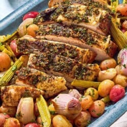 A close up photo of a sliced roast turkey breast with grapes and vegetables on a serving platter.