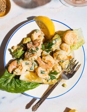 Overhead shot of a serving of shrimp salad on a plate with a lemon wedge on the side.