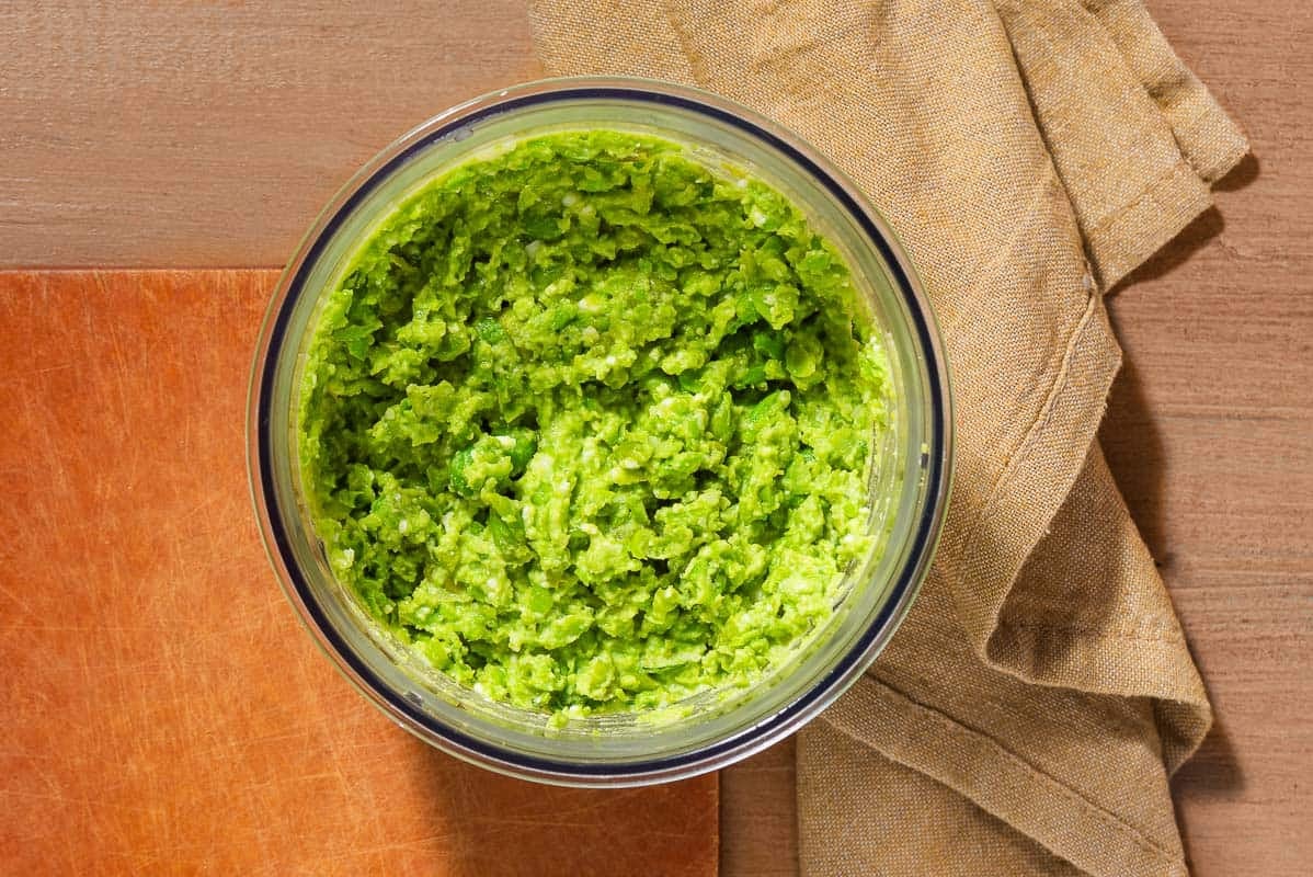 An overhead photo of smashed peas in a bowl next to a cloth napkin.