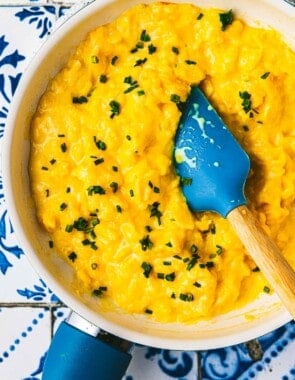 soft scrambled eggs topped with chives being stirred with a spatula in a saucepan.