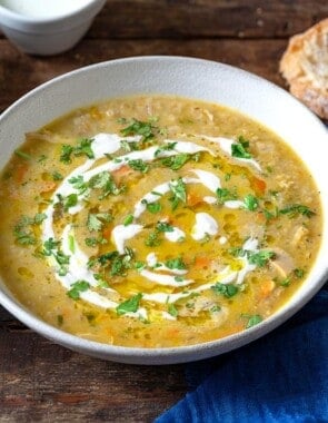 soupe jo in a bowl garnished with half and half and chopped parsley, surrounded by small bowls of olive oil, chopped parsley and half and half, and slices of crusty bread.