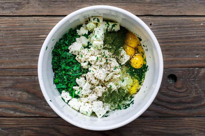 Spanakopita filling ingredients in a bowl. Spinach, feta, fresh herbs, onions, garlic and eggs