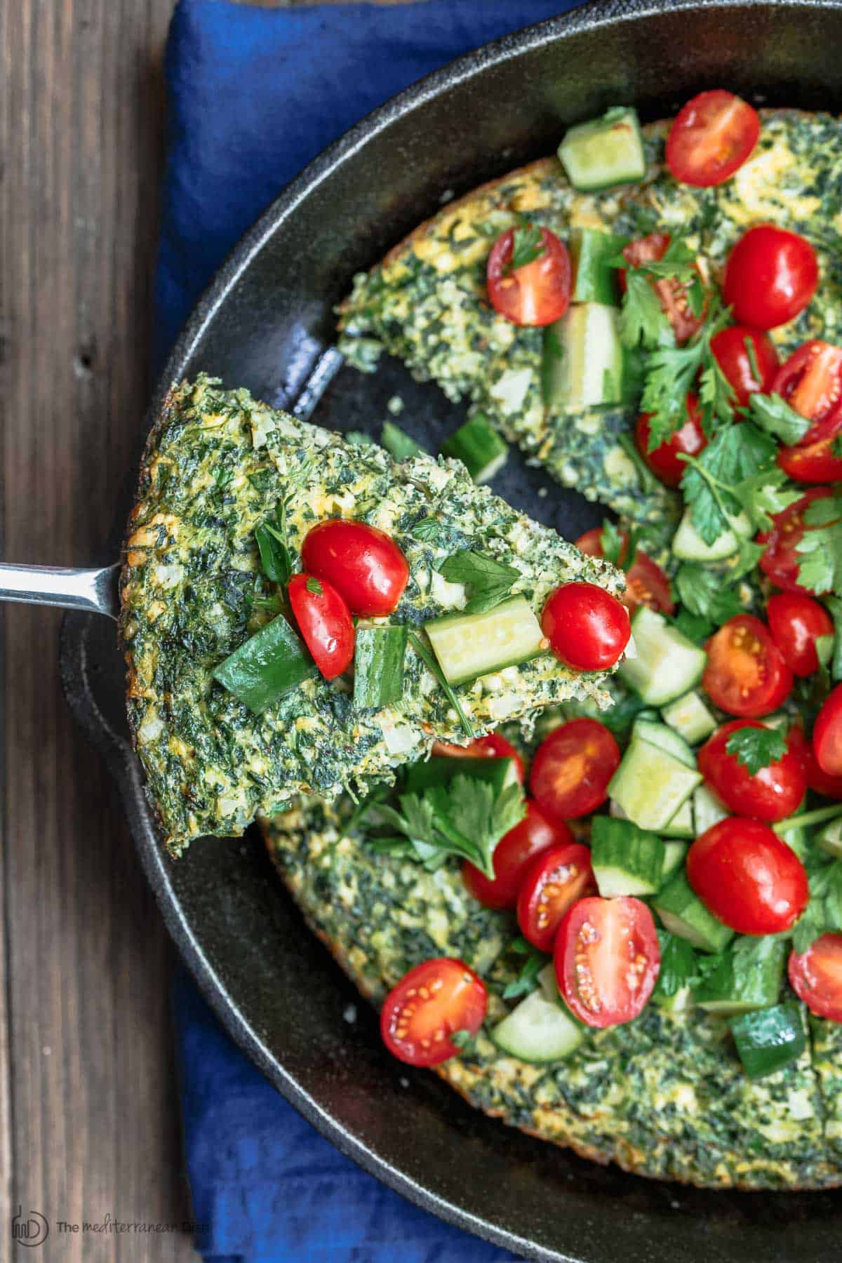 A slice of spinach frittata being served with Mediterranean salad