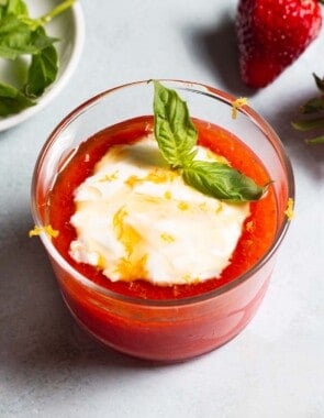 Close up of strawberry pudding with a dollop of Crème fraîche, drizzle of honey, lemon zest and a sprig of basil.