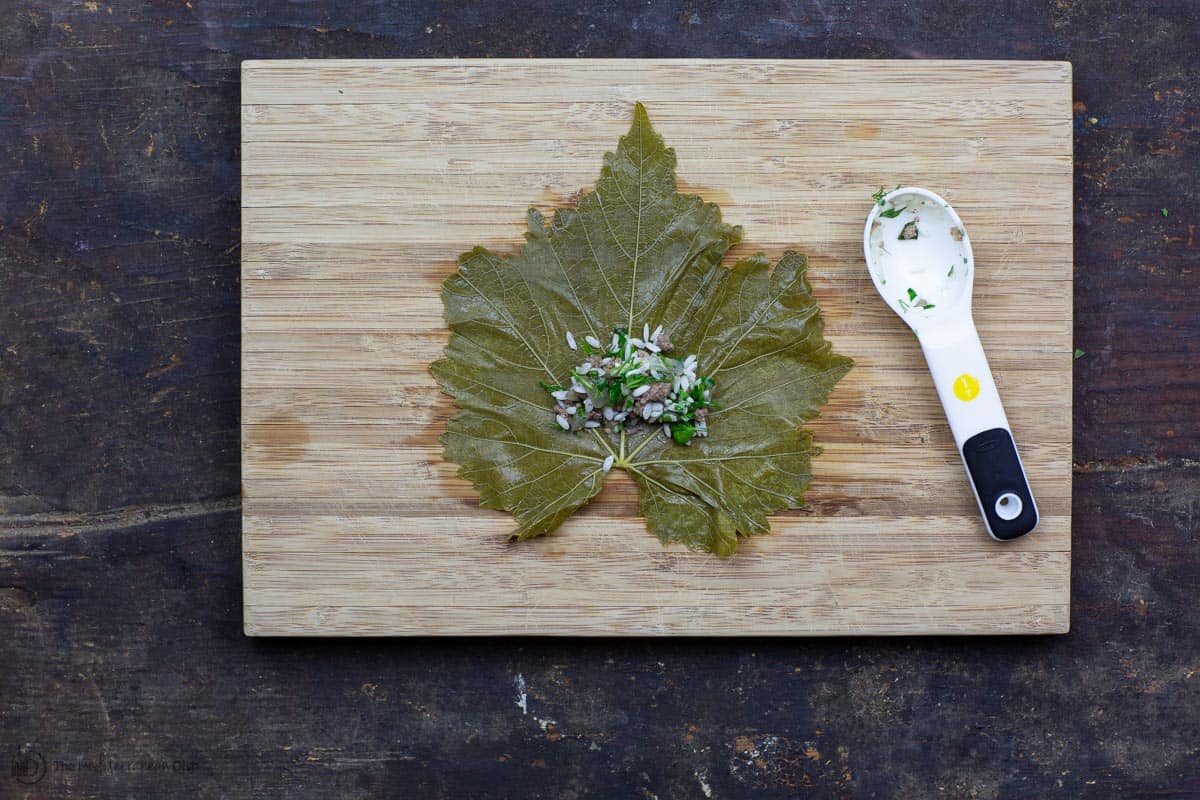 One grape leaf on cutting board with rice stuffing in middle