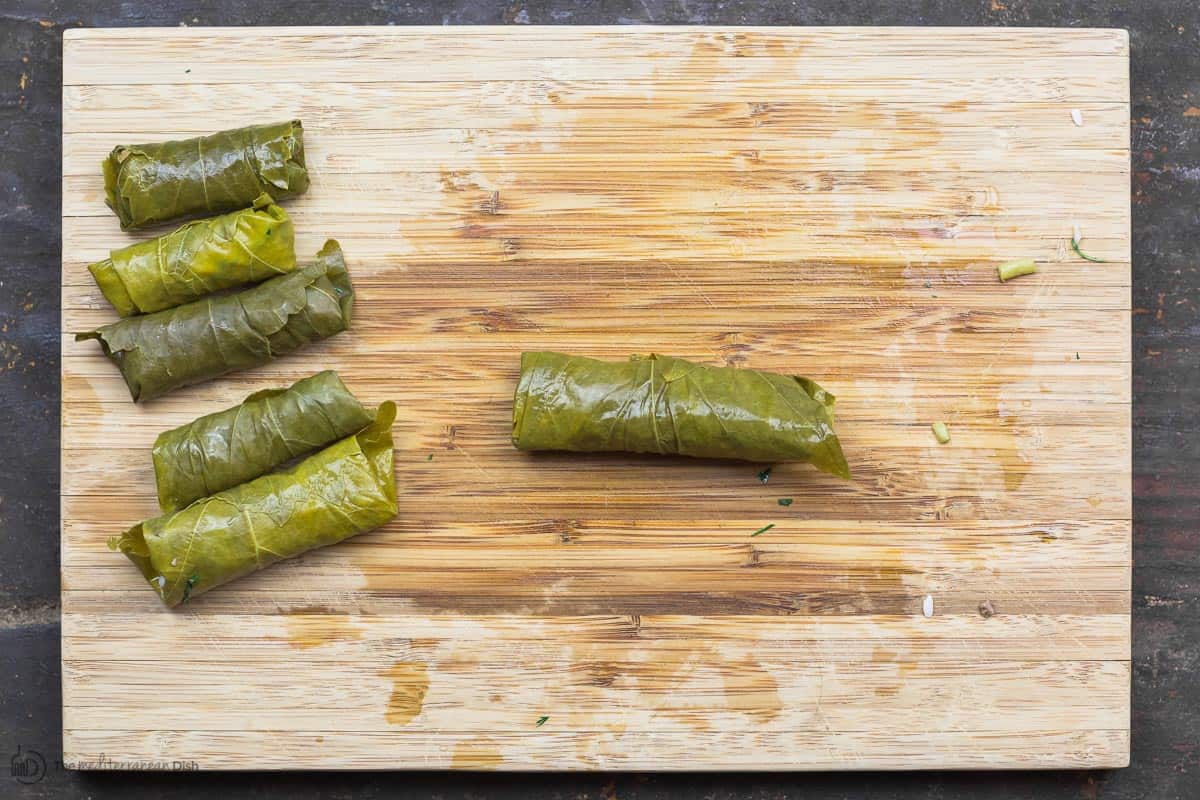 A few fully rolled stuffed grape leaves on cutting board