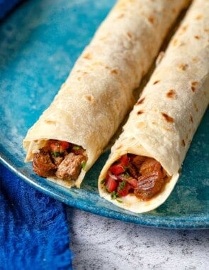 close up shot of the top of two tantuni steak wraps, showing the steak and tomato salad.