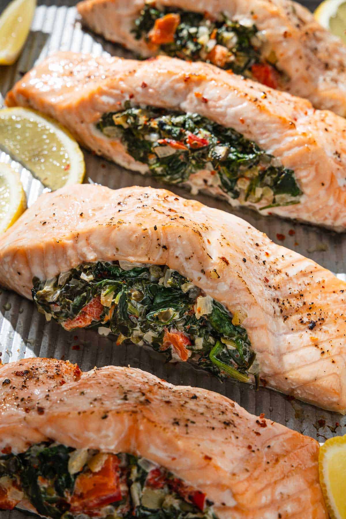 A close up of 4 cooked stuffed salmon fillets on a baking sheet with lemon wedges.