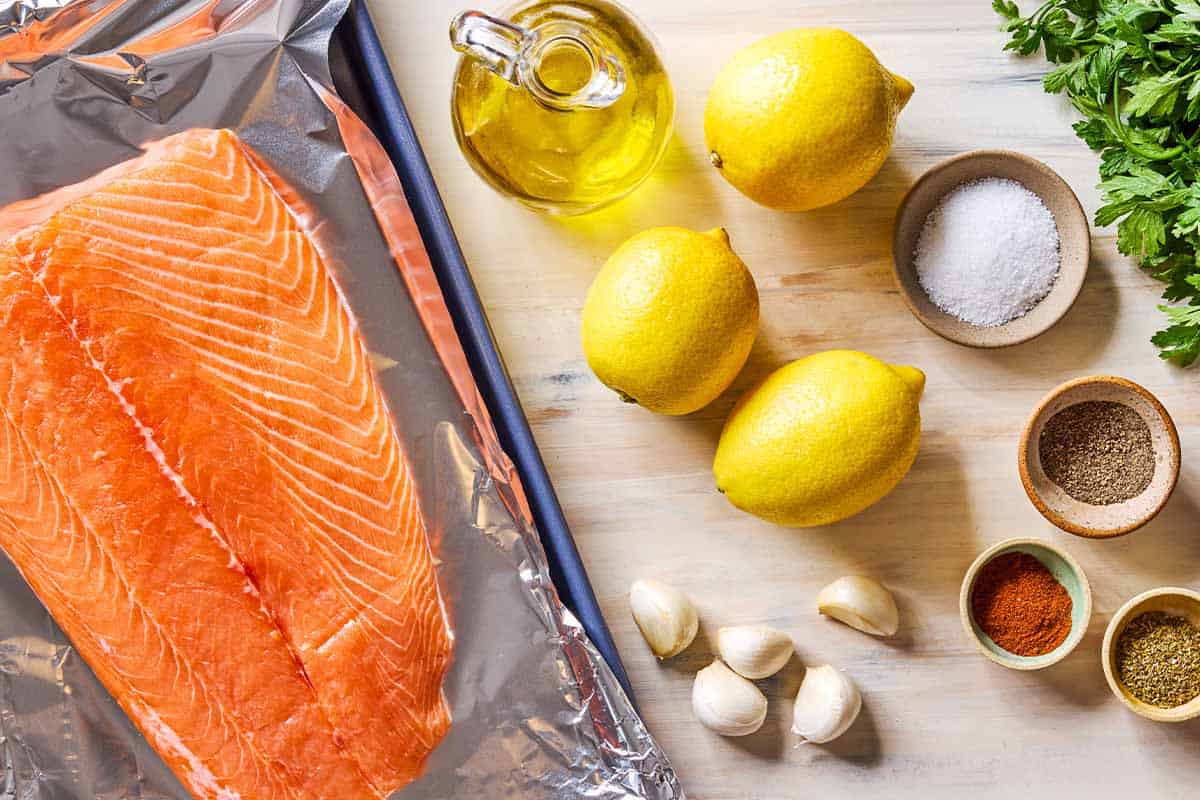 Ingredients for lemon garlic salmon including lemons, garlic, salmon, olive oil, salt, parsley, oregano, paprika and black pepper.