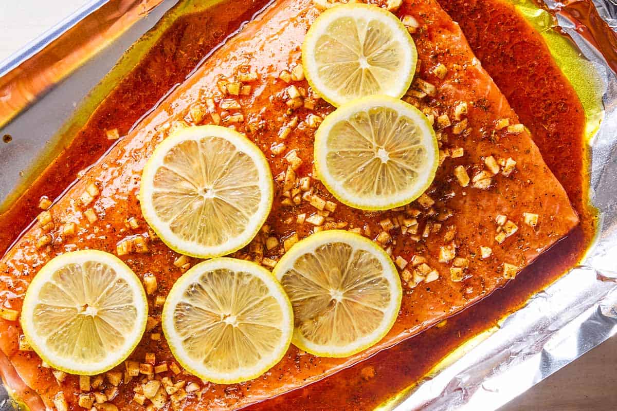 An overhead close up photo of an unbaked lemon garlic salmon fillet topped with lemon wheels on an aluminum foil-lined sheet pan.