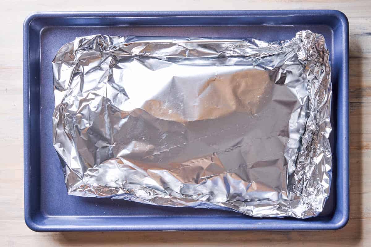 An overhead photo of a lemon garlic salmon fillet wrapped in aluminum foil on a sheet pan.