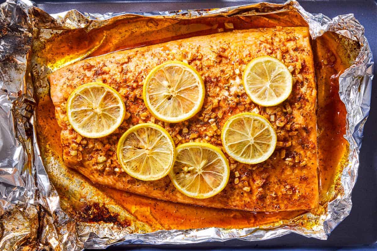 An overhead photo of a lemon garlic salmon fillet topped with lemon wheels on an aluminum foil-lined sheet pan.