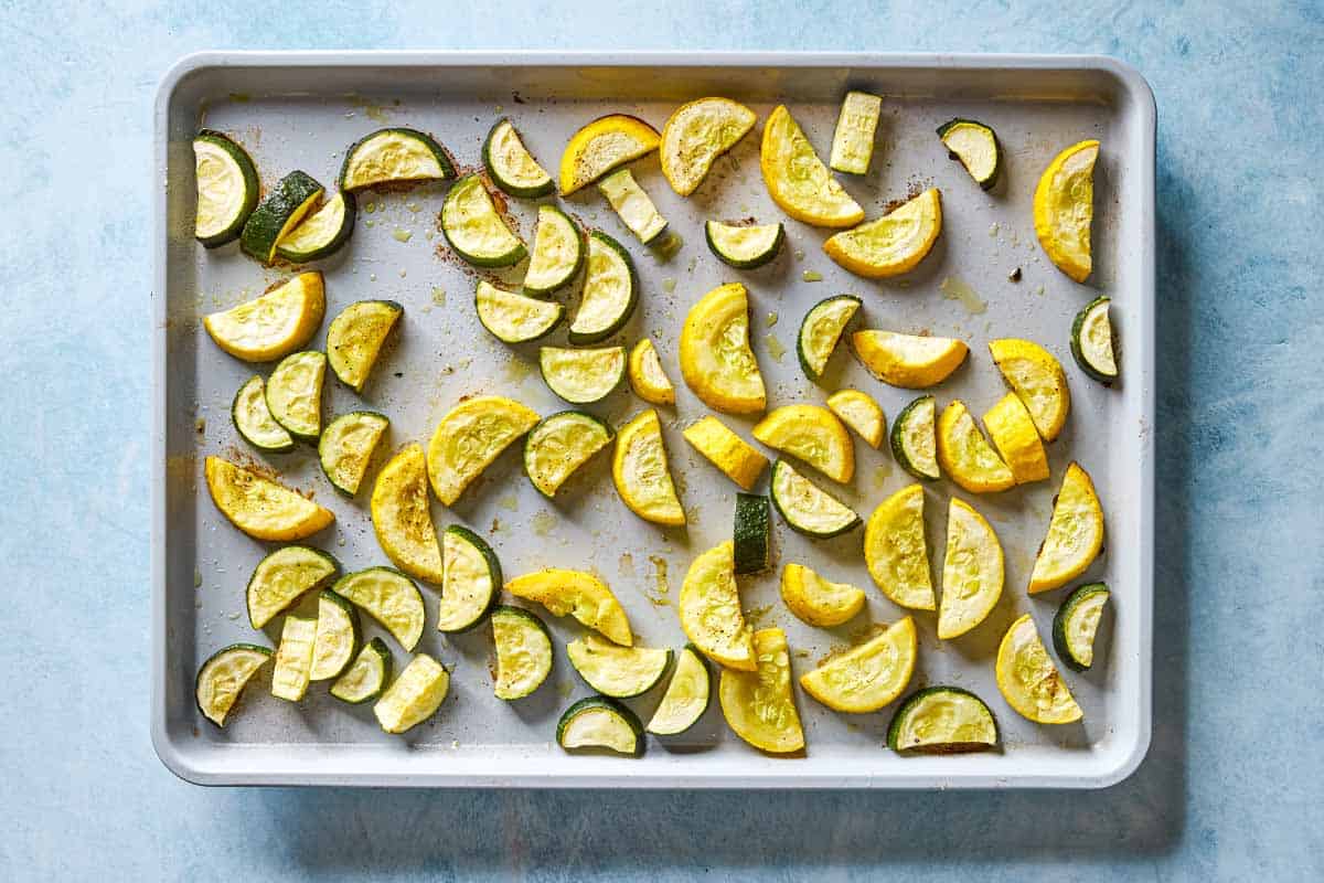 Slices of roasted zucchini spread evenly on a sheet pan.