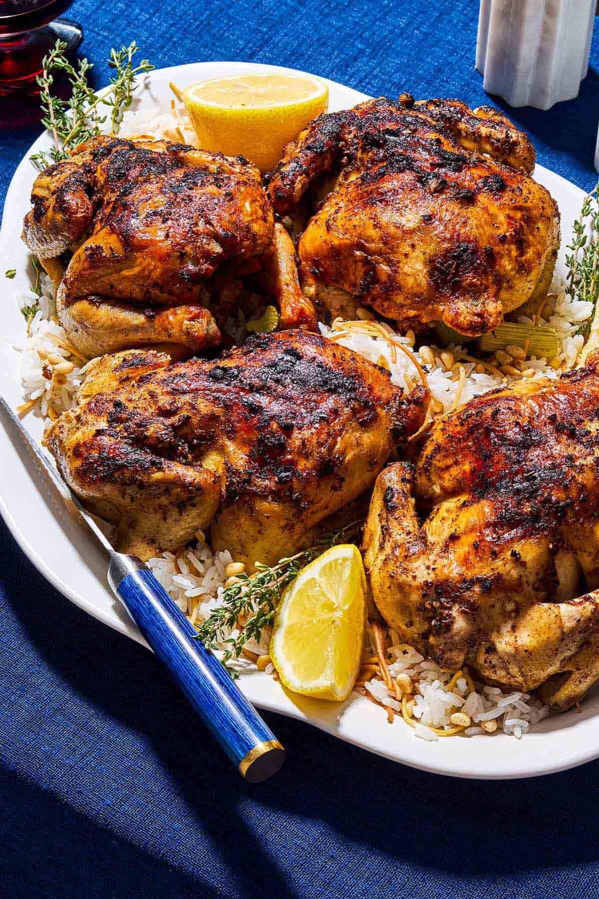 4 roasted cornish hens on a bed of rice on a serving platter with lemon wedges and a knife.