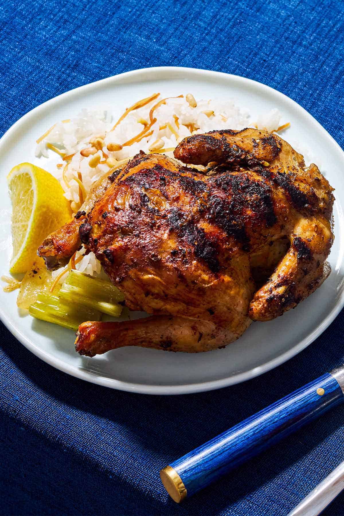 A roasted cornish hen on a plate with a lemon wedge and a side of rice.