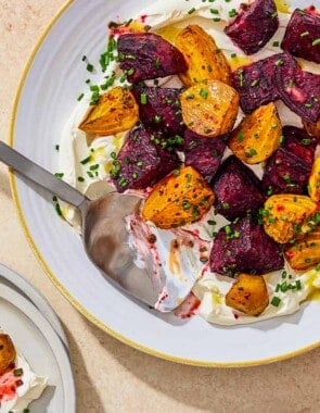 An overhead photo of roasted beets on a layer of labneh spread on a platter and topped with chives and a drizzle of apple cider vinaigrette with a serving spoon. Next to this is a serving of the roasted beets on a plate.