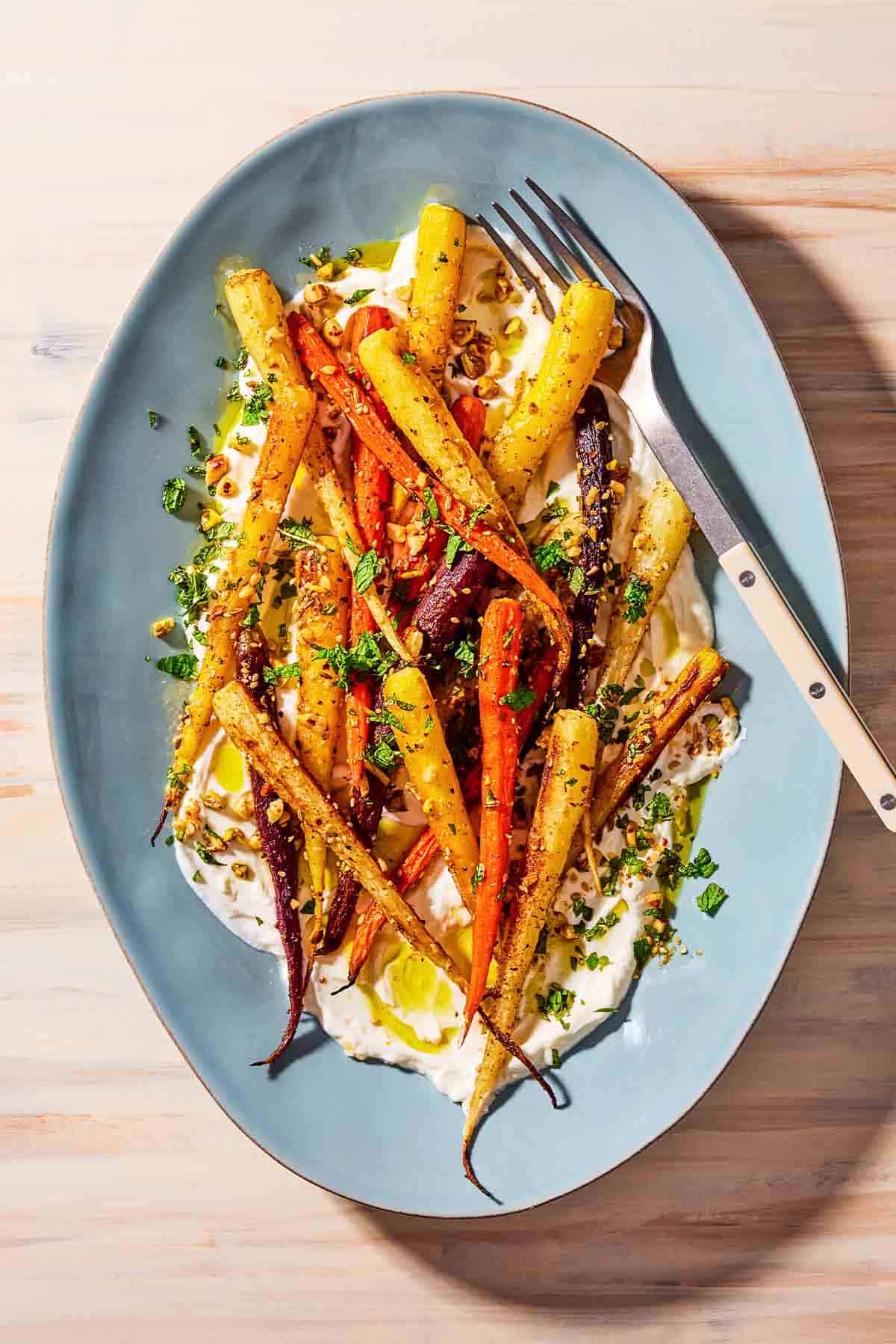 An overhead photo of roasted rainbow carrots with with dukkah, mint and a garlicky yogurt sauce on a serving platter with a fork.