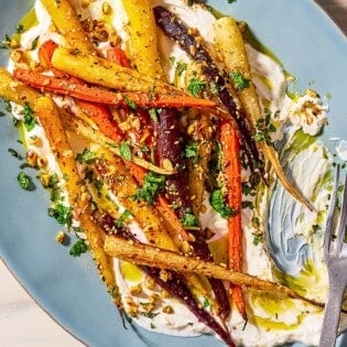 An overhead close up of roasted rainbow carrots with with dukkah, mint and a garlicky yogurt sauce on a serving platter with a fork.