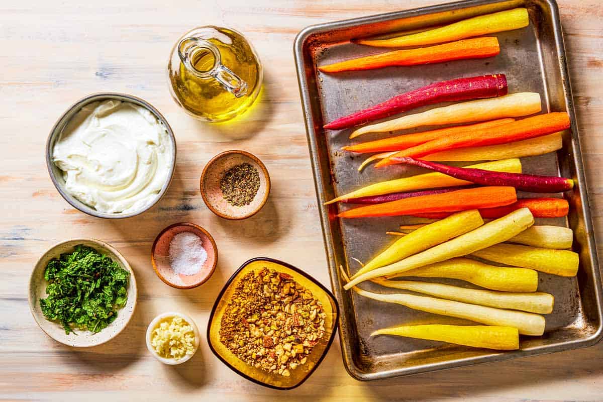 ingredients for roasted rainbow carrots including rainbow carrots, olive oil, salt, pepper, dukkah, greek yogurt, garlic, and chopped mint.