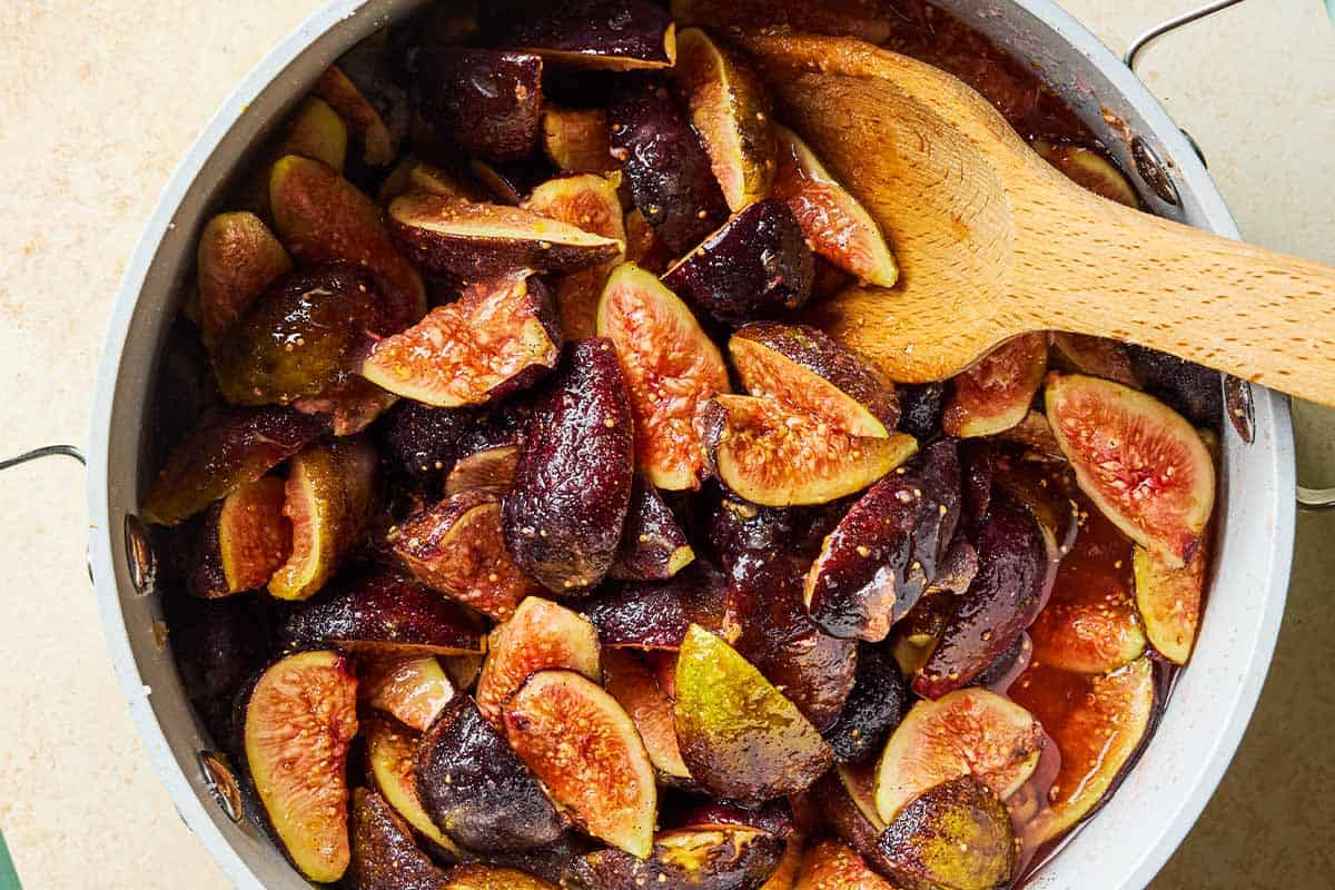 Figs cooking in a pot with a wooden spoon.