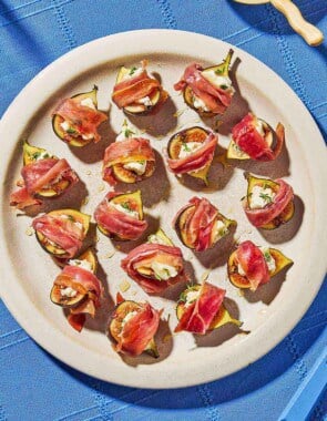 An overhead photo of several prosciutto wrapped figs drizzled with honey on a plate next to a bowl of honey.