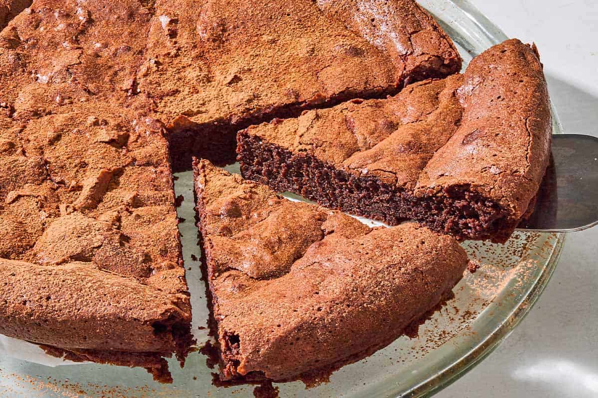 A close up of the flourless chocolate cake with 2 slices cut on a serving platter.