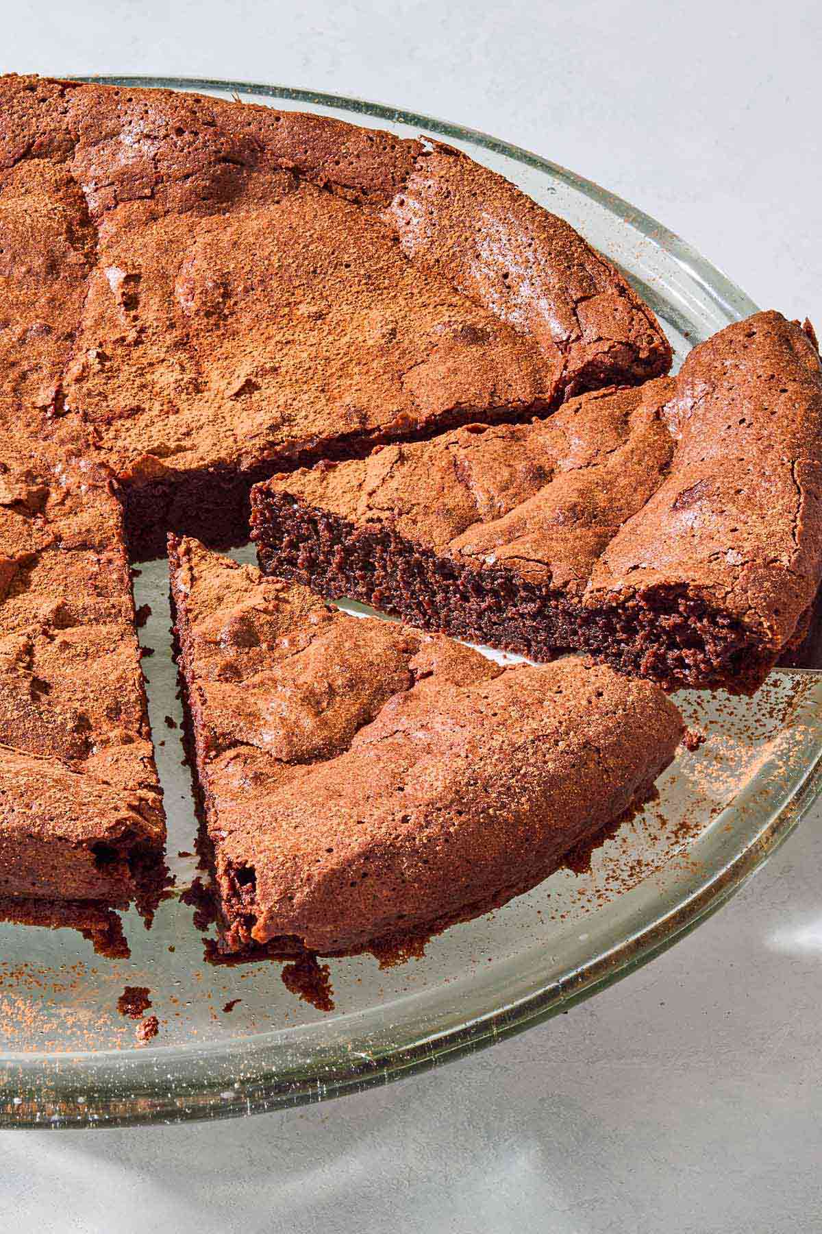 A close up of the flourless chocolate cake with 2 slices cut on a serving platter.