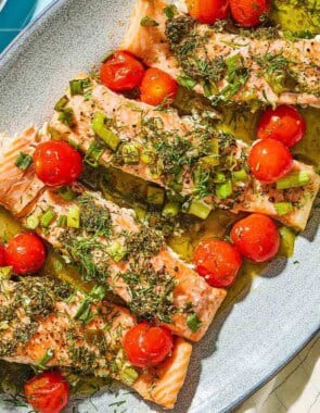 A close up of 4 Greek salmon fillets with cherry tomatoes on a platter.