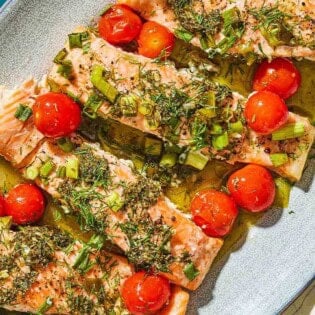 A close up of 4 Greek salmon fillets with cherry tomatoes on a platter.