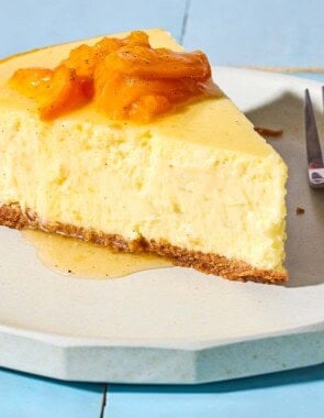 A close up of a slice of the greek yogurt cheesecake topped with the apricot, vanilla and honey compote on a plate with a fork.