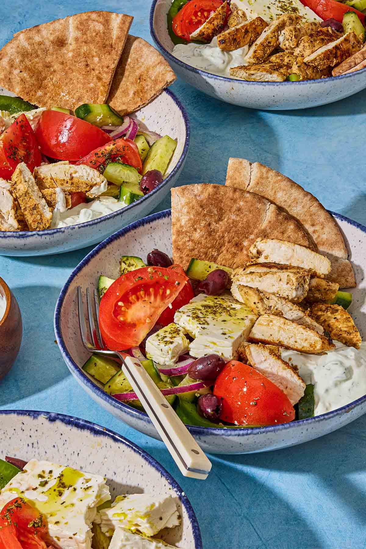 A close up of 4 gyro bowls one on a blue background. One bowl has a fork.