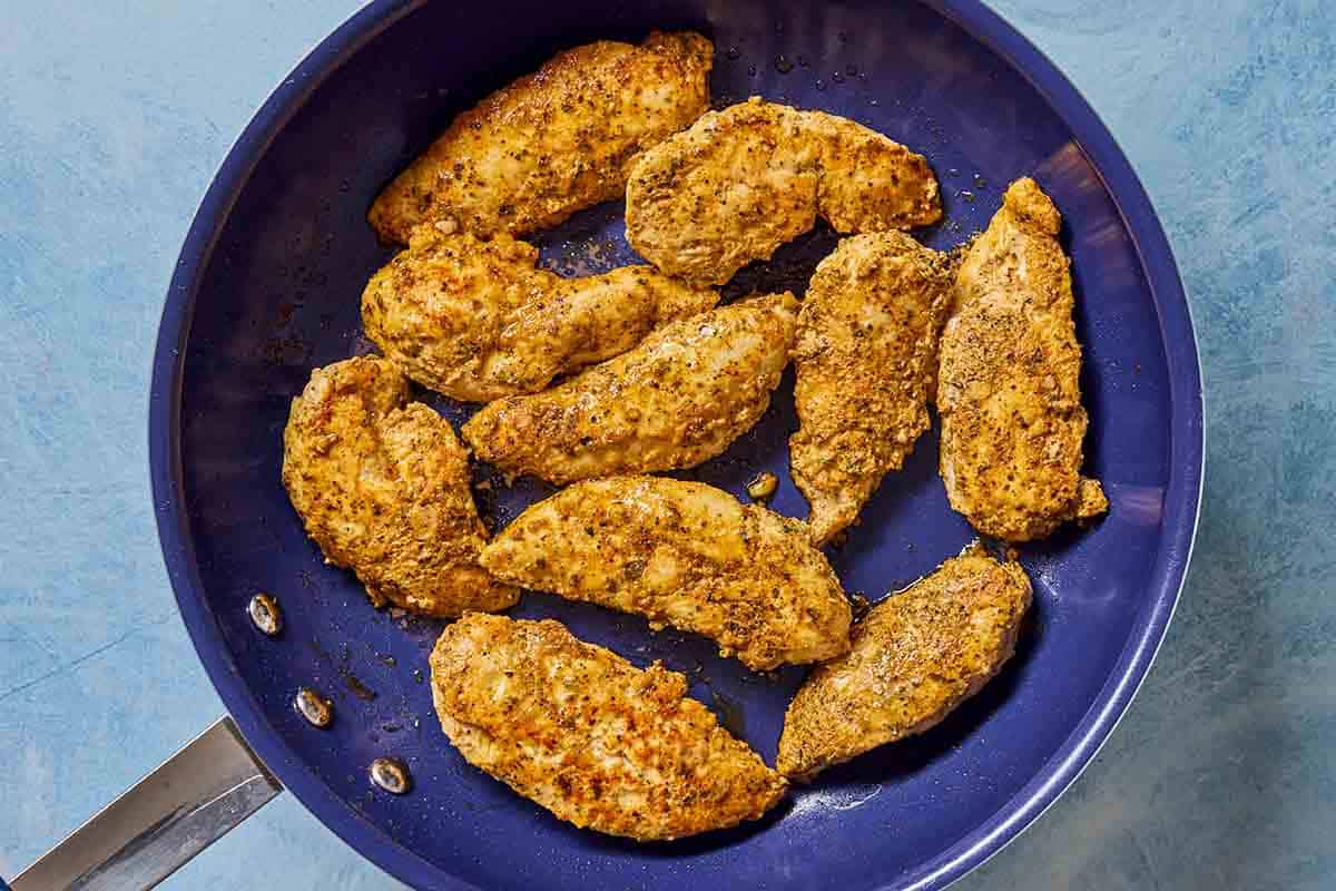 Marinated chicken tenderloins cooking in a skillet.