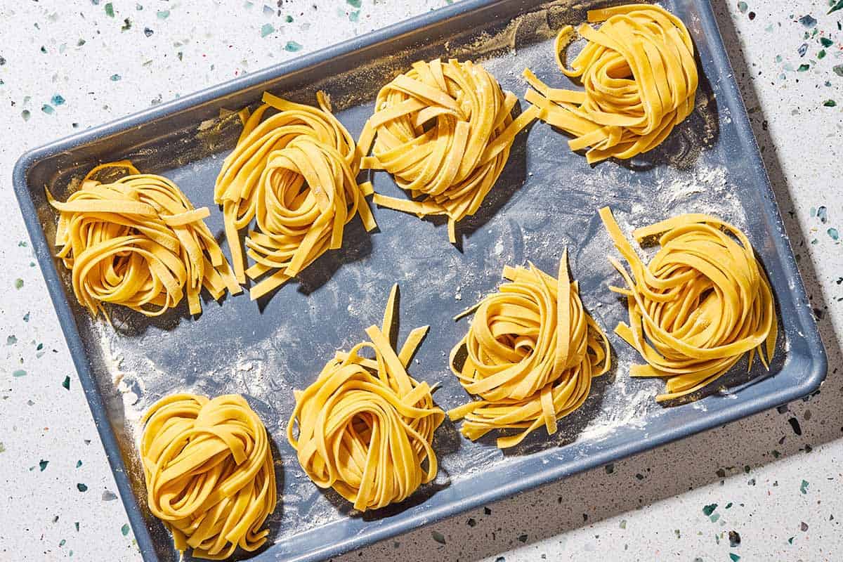 An overhead photo of uncooked homemade pasta noodles formed into 8 nest shapes.