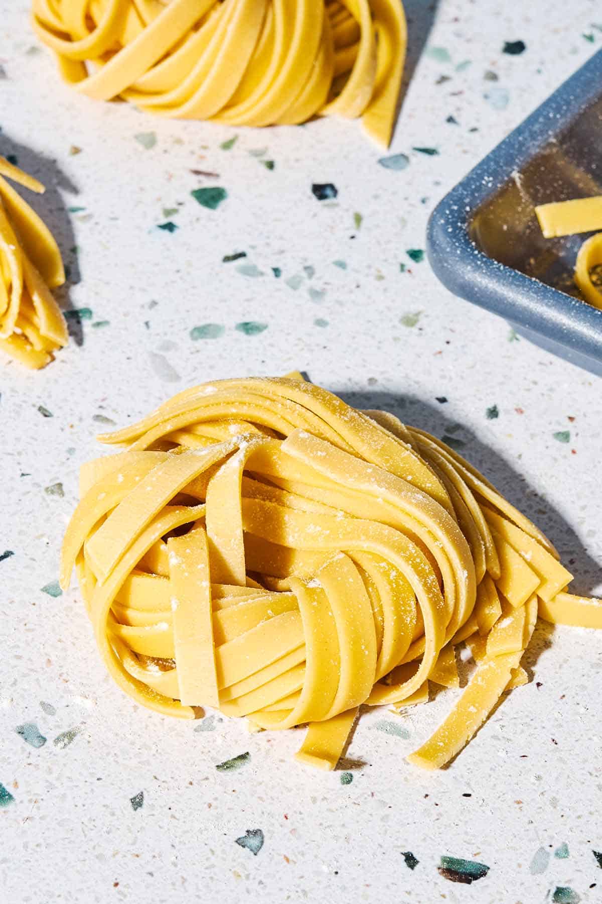 A close up photo uncooked homemade pasta noodles formed into the shape of a nest.