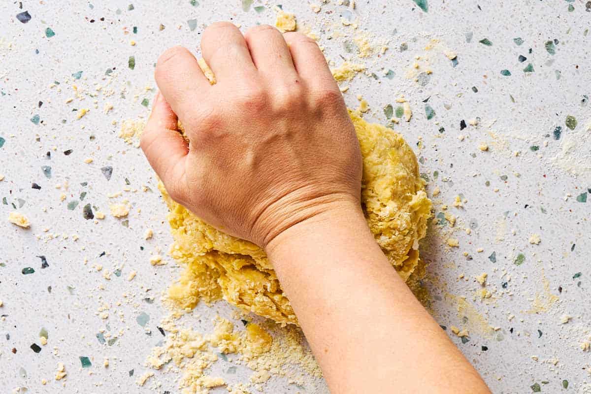 An overhead photo of a hand kneading a ball of dough.