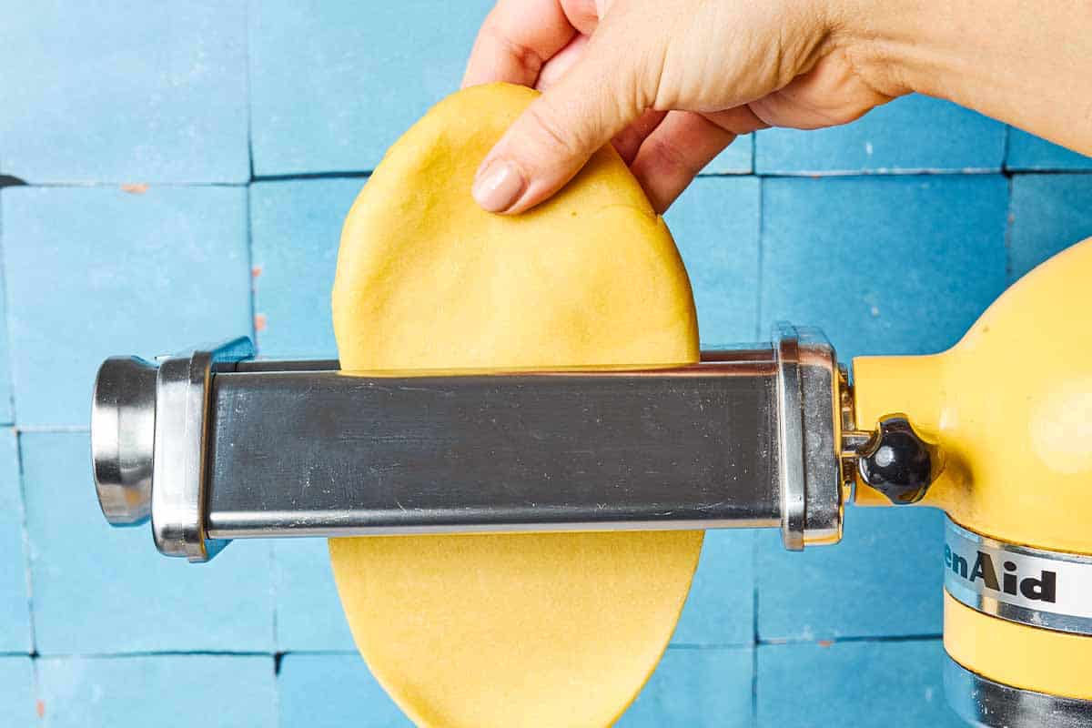 A close up of a homemade pasta dough being stretched through the rollers of a pasta machine.