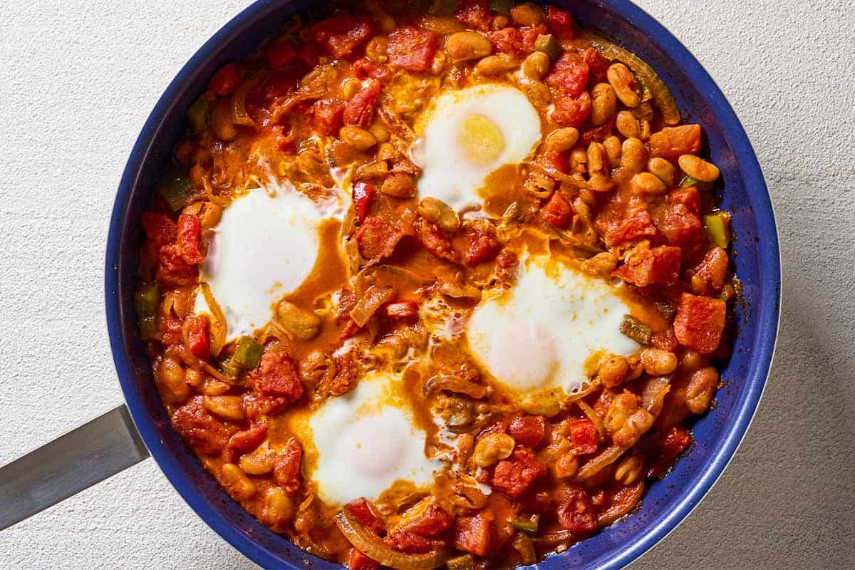 An overhead photo of 4 eggs cooking in the white bean shakshuka sauce in a skillet.