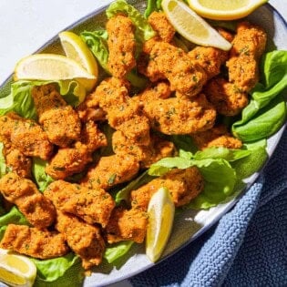 An overhead photo of several turkish lentil patties with lettuce and lemon wedges on a serving platter with a kitchen towel.