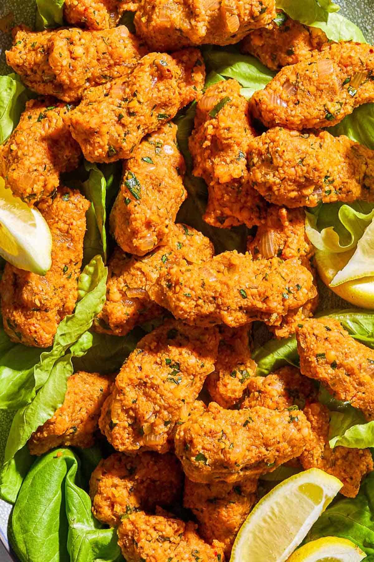 A close up of several turkish lentil meatballs called Mercimek Köftesi with lettuce and lemon wedges.